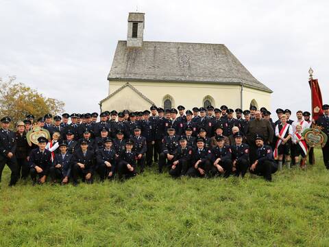 Gruppenbild der freiwilligen Feuerwehr Endlhausen mit Vereinsfahne. Die Mitglieder sind in Uniform gekleidet. Im Hintergrund sieht man die Kapelle von Eulenschwang